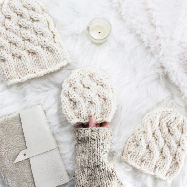 baby cable knit hat with adult and teen hats displayed on faux fur blanket