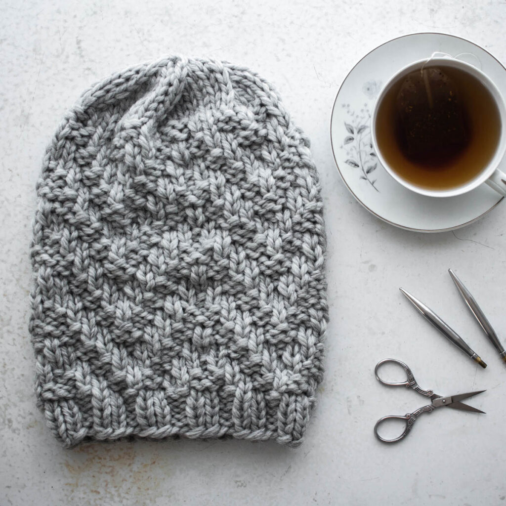 chevron knit hat displayed table with a cup of tea, scissors and knitting needles