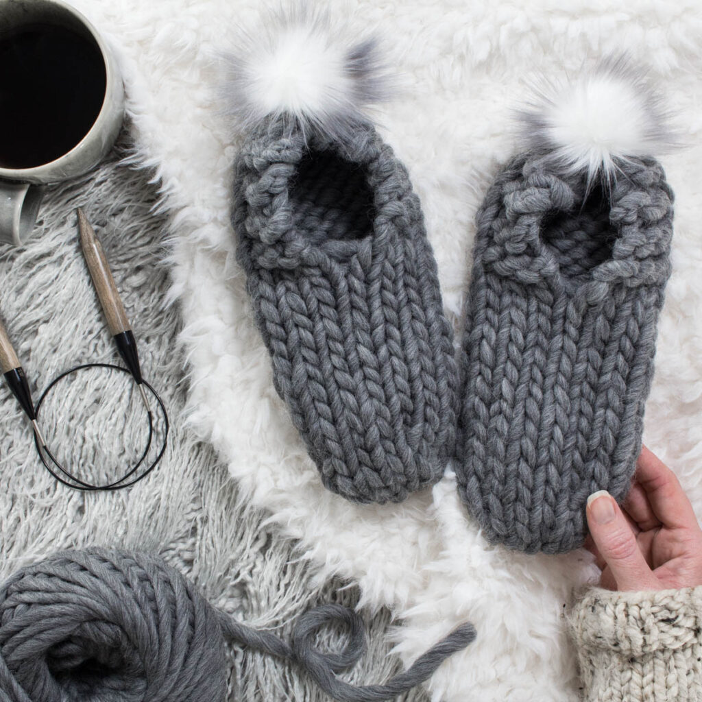 Chunky Knit Slippers on a faux fur blanket with yarn, needles & coffee mug