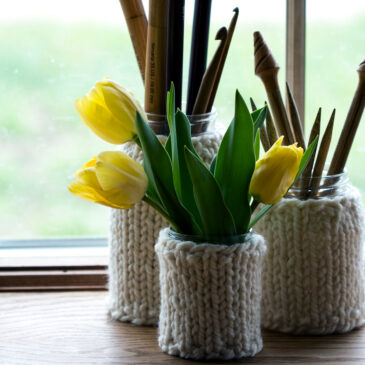 3 Mason Jar Cozies displayed on a mason jars with tulips & wooden knitting needles